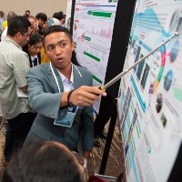 A presenter uses a pointer to refer to a science poster board, as he explains what is on it to other people.