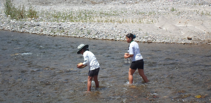 Two girl students wade in a stream and gather water samples.