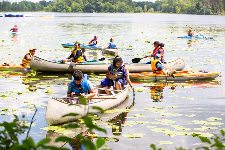 Students in kayaks taking water samples and testing the water with scientific instruments.