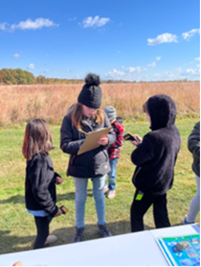 Students students holding infrared thermometers to measure surface temperature share their readings with another student holding a clipboard
