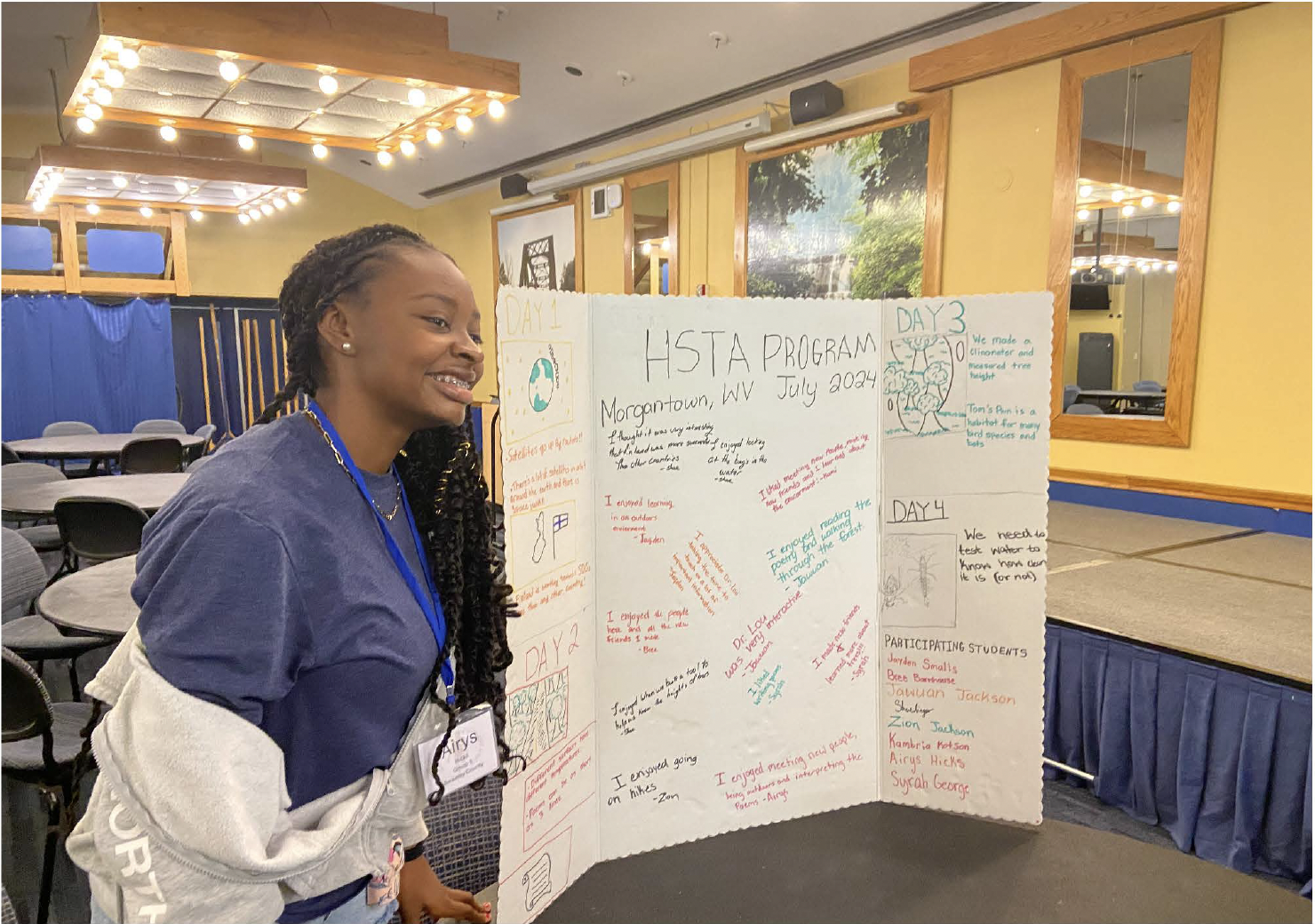 a student poses by a tri-fold board with notes from students who attended the GLOBE camp