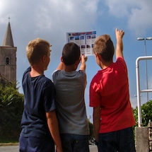 Three children look at a cloud chart while one points at the sky.