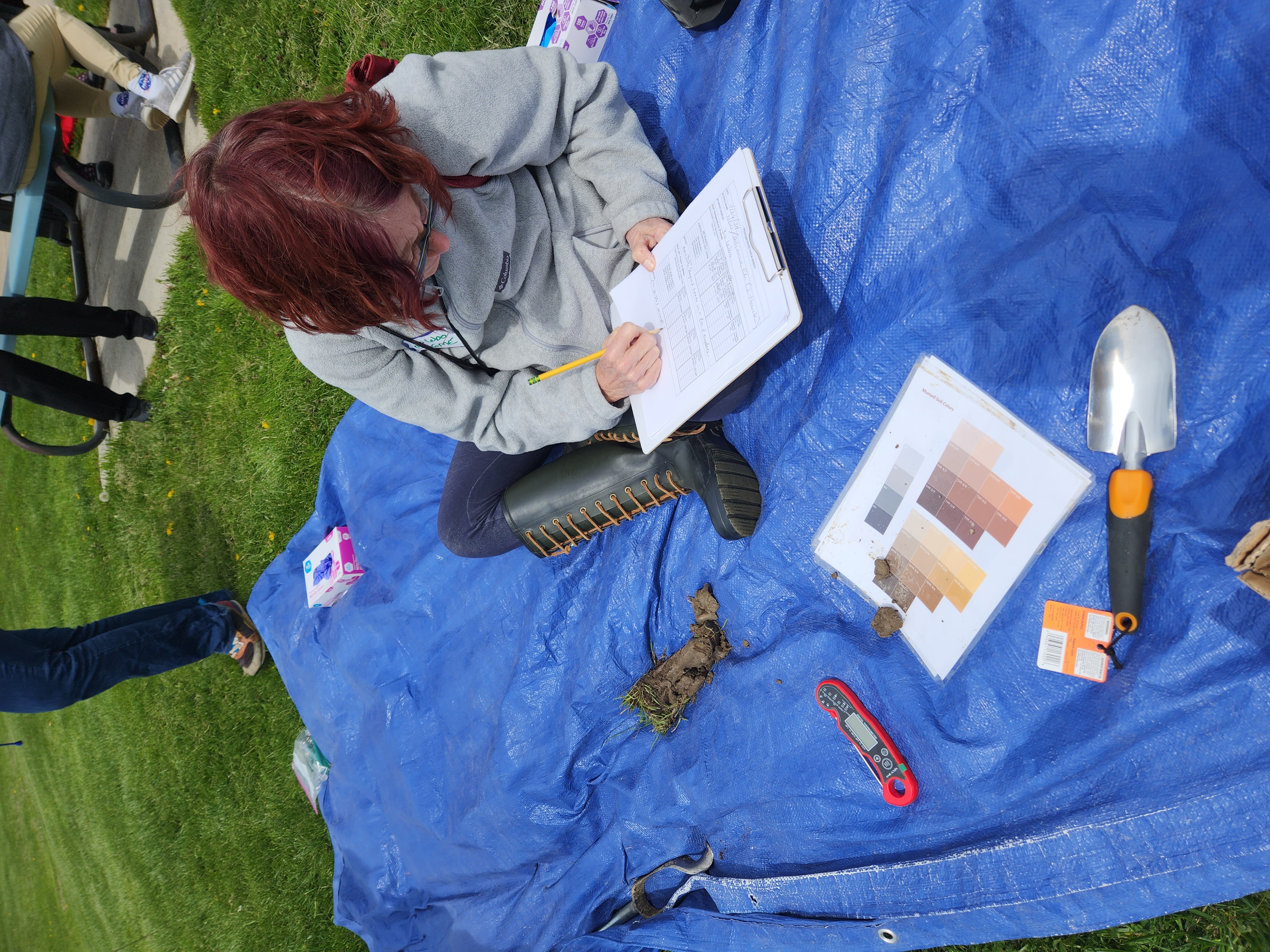 Bo Lebo sits on a tarp on the ground to make observations of a soil sample