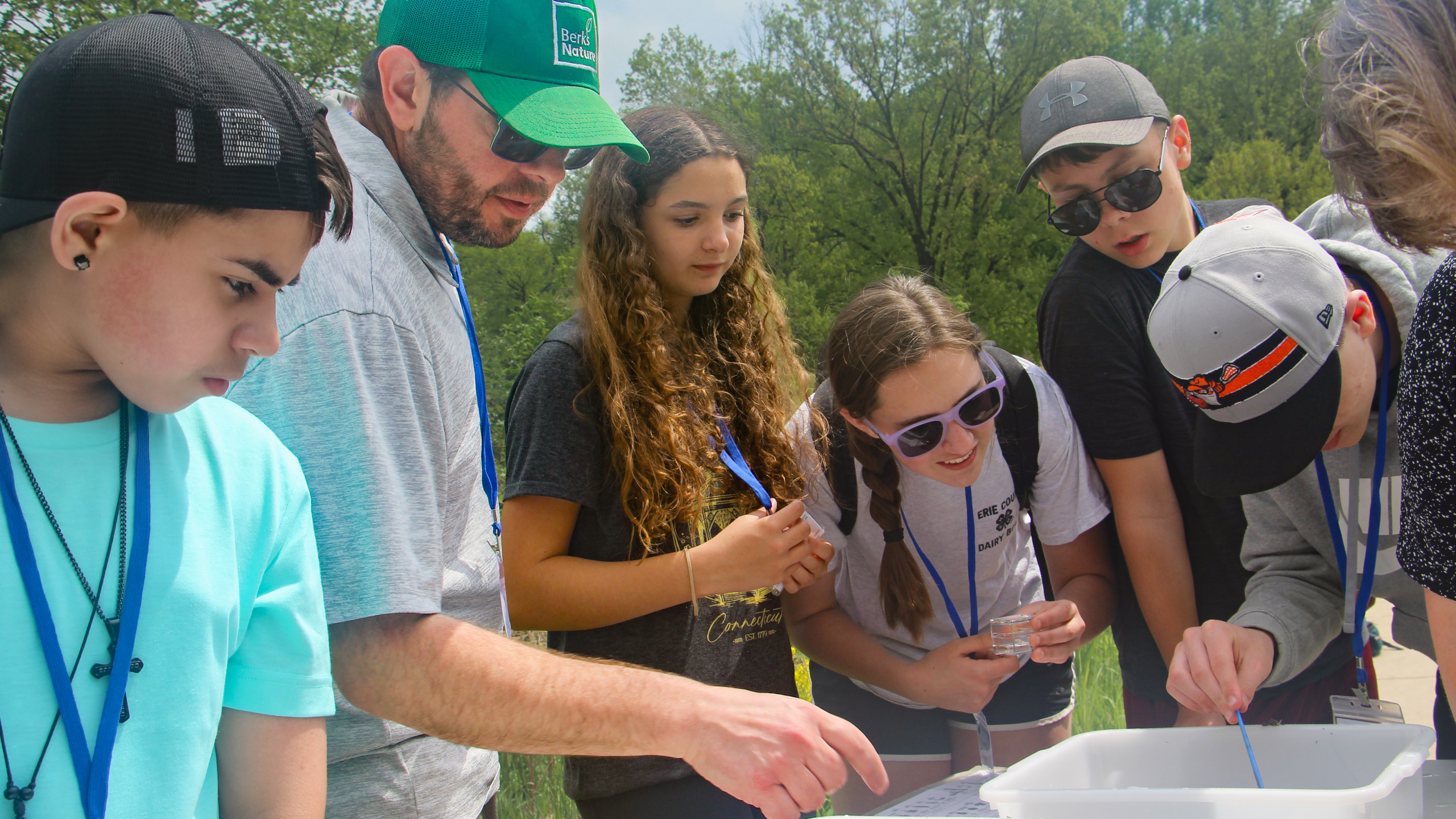 students and GLOBE Partner Michael Griffith stand around a table with white tubs filled with aquatic macroinvertebrates in white tubs