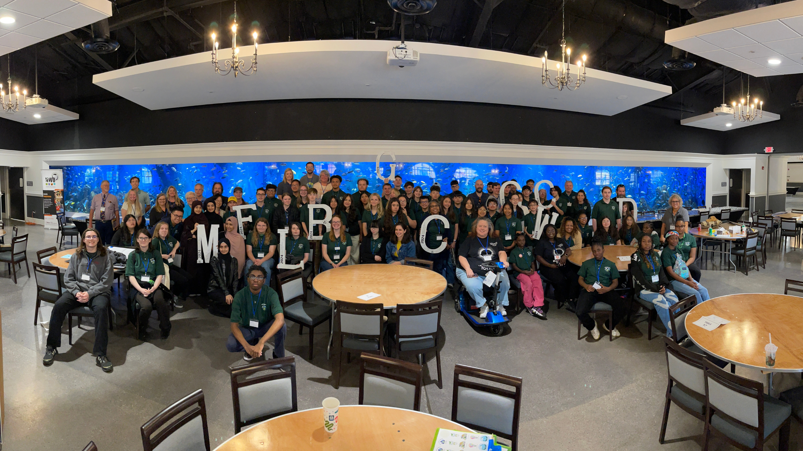 GLOBE students, educators and Partners pose in front of a fish tank in a meeting space at the Toledo Zoo and Aquarium