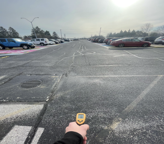 a hand points an infrared thermometer at a parking lot to measure surface temperature