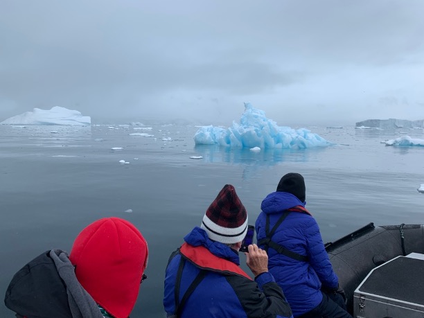 A photograph of people on a raft taking cell phone photos of icebergs.