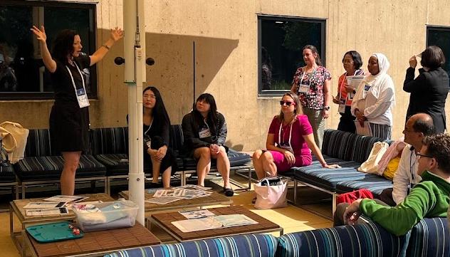 A gathering of people in an outdoor seating area. One woman is standing at the side with her arms up explaining something.