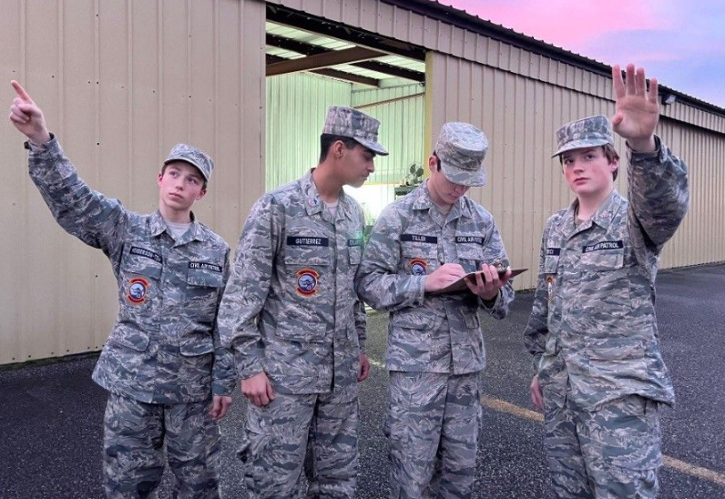 Civil Air Patrol cadets standing in front of an airplane hangar looking at the sky