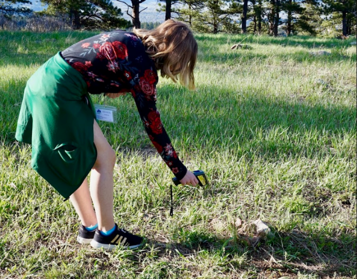 girl measuring surface temperature of grassy area