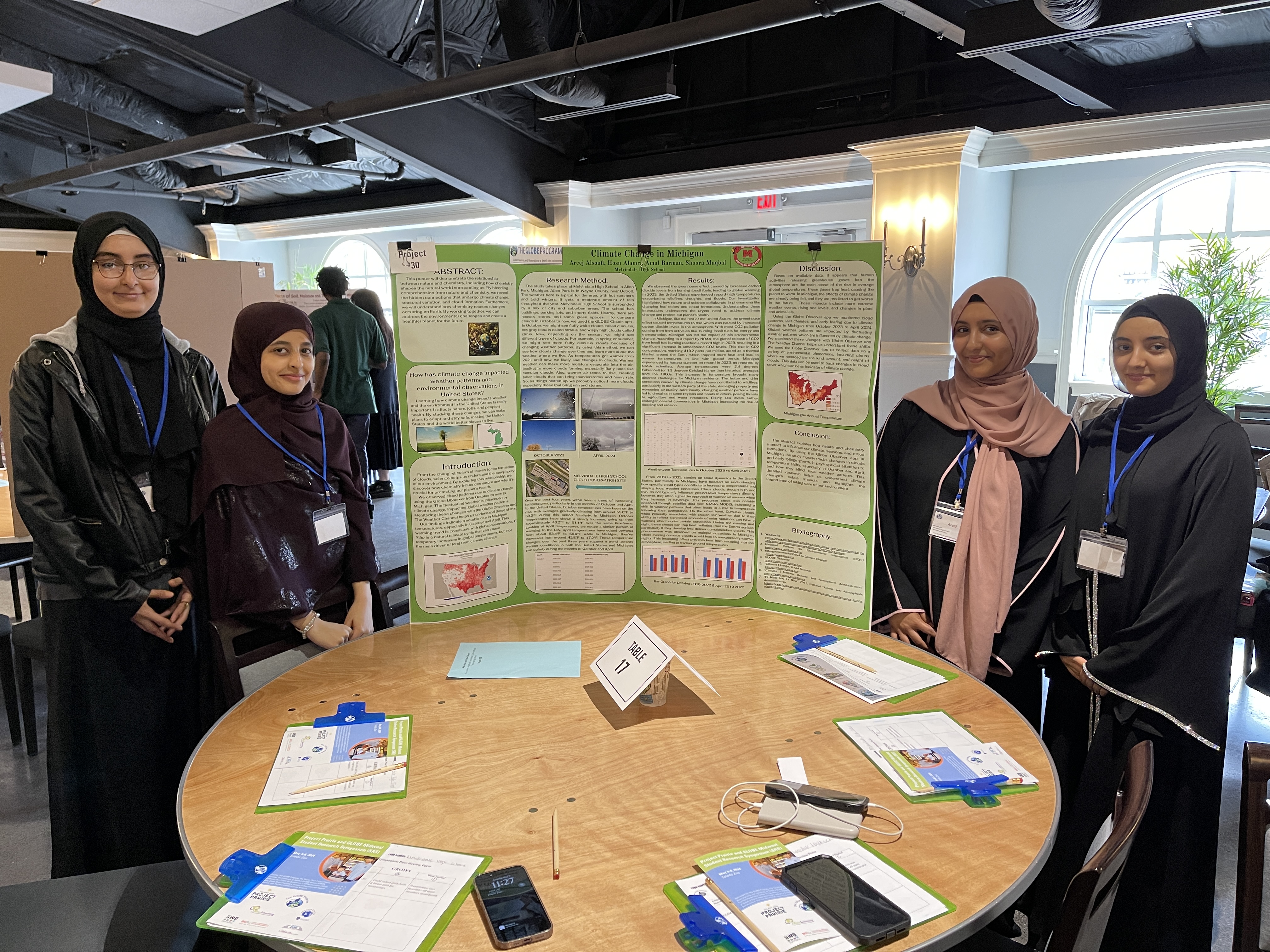 Four students smile by their poster